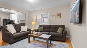 Ein Wohnzimmer mit zwei Sofas, einem Couchtisch und einem Teppich. Im Hintergrund ist eine Küche zu sehen.