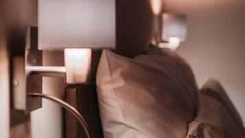 A close-up of a bed with a headboard, a wall-mounted lamp, and a framed picture above the bed.