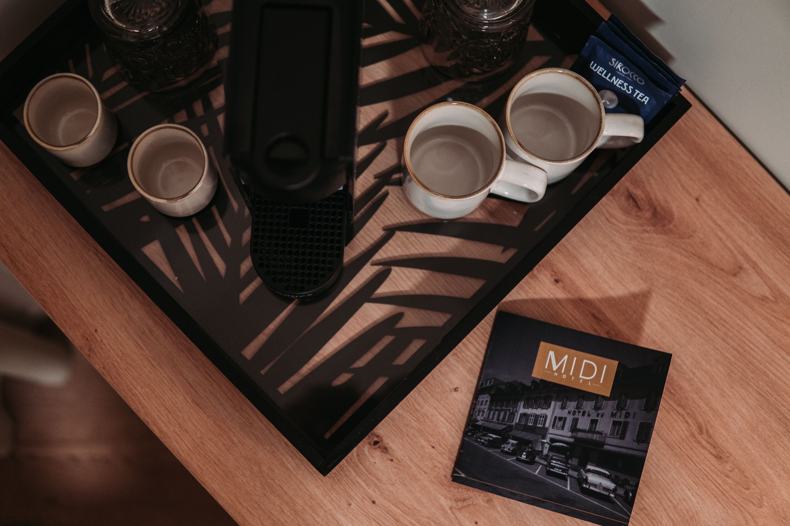 A tray with four cups and a hairbrush, a bottle of wellness tea, and a brochure for Midi Hotel.