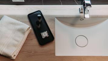 Uma mesa de madeira com um smartphone, um pequeno bandeja com duas garrafas e uma pia branca.