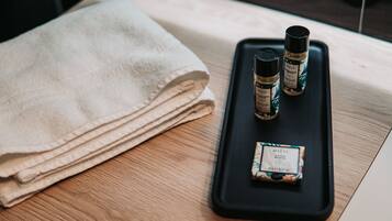 A neatly folded beige towel on a wooden table with a black tray containing two bottles of Balja body care products and a small box.