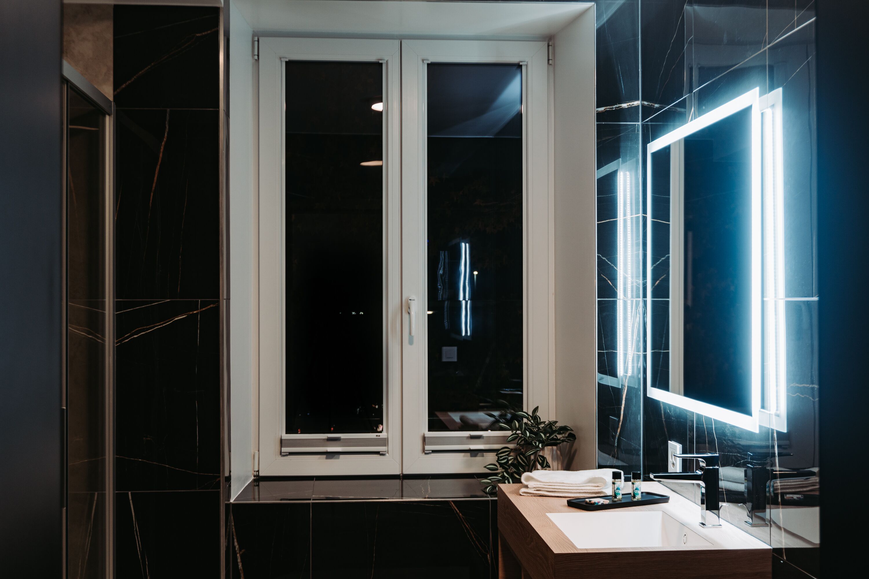 Une salle de bain moderne avec un sol en marbre foncé, un lavabo blanc et un grand miroir.