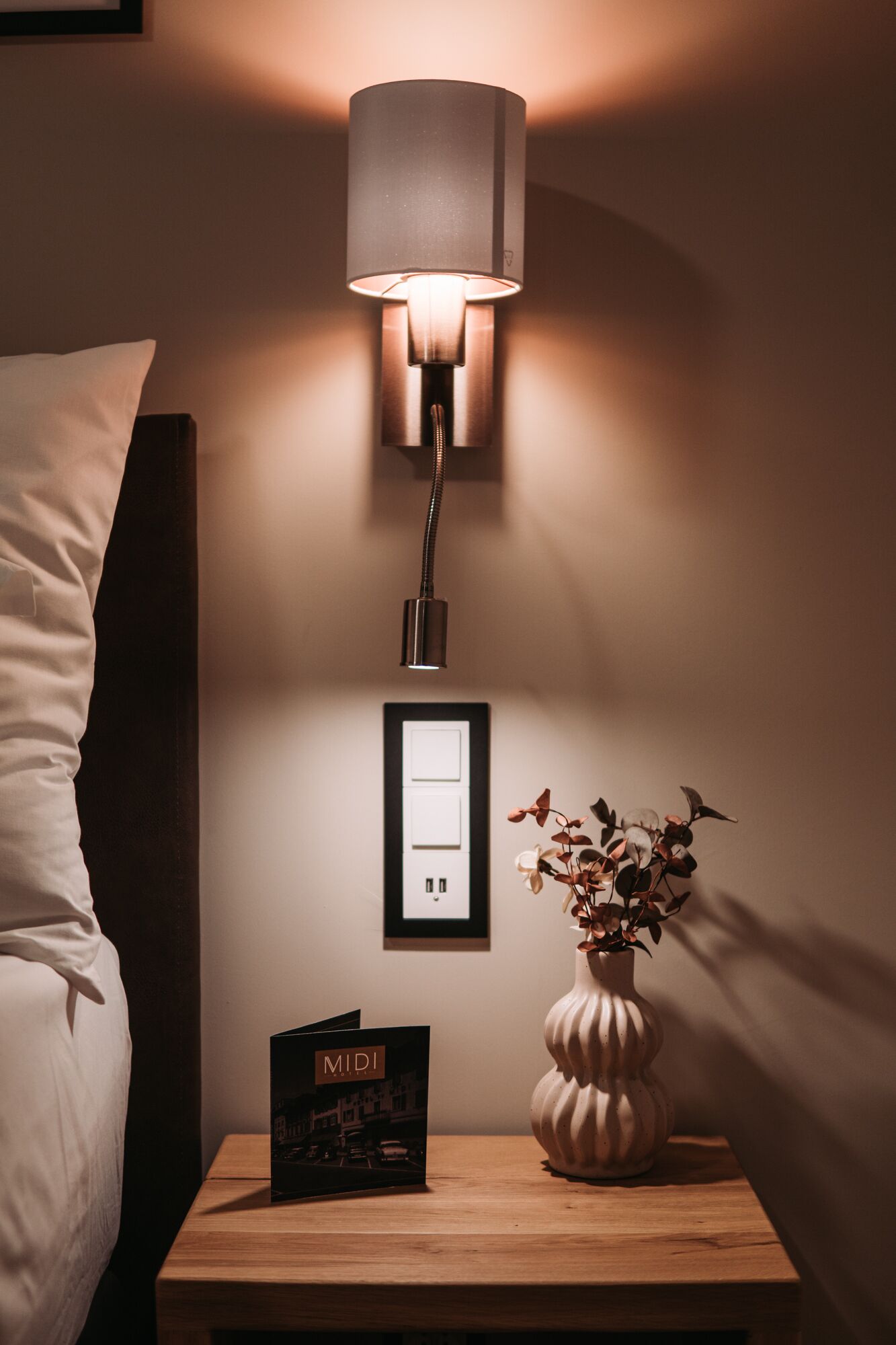 Ein Nachttisch mit Lampe, einem gerahmten Bild, einer Blumenvase und einer Zeitschrift.