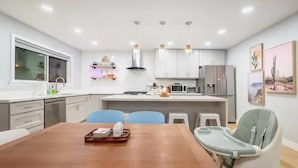 A modern kitchen with white cabinets, a wooden dining table, and a high chair.