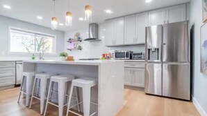 A modern kitchen with a central island, bar stools, stainless steel appliances, and pendant lighting.