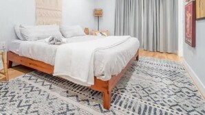 A bedroom with a wooden bed, white bedding, a patterned rug, and a large wall tapestry.