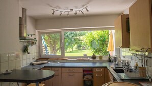 Een keuken met een groot raam, houten kastjes, een zwart aanrecht en een kleine eettafel.
