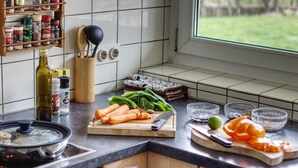 Een keuken met een fornuis, een snijplank met groenten, een mes en een raam met uitzicht op een tuin.