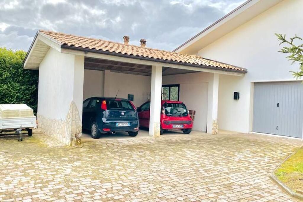 A covered parking area with two cars parked inside, a white trailer, and a grey garage door.