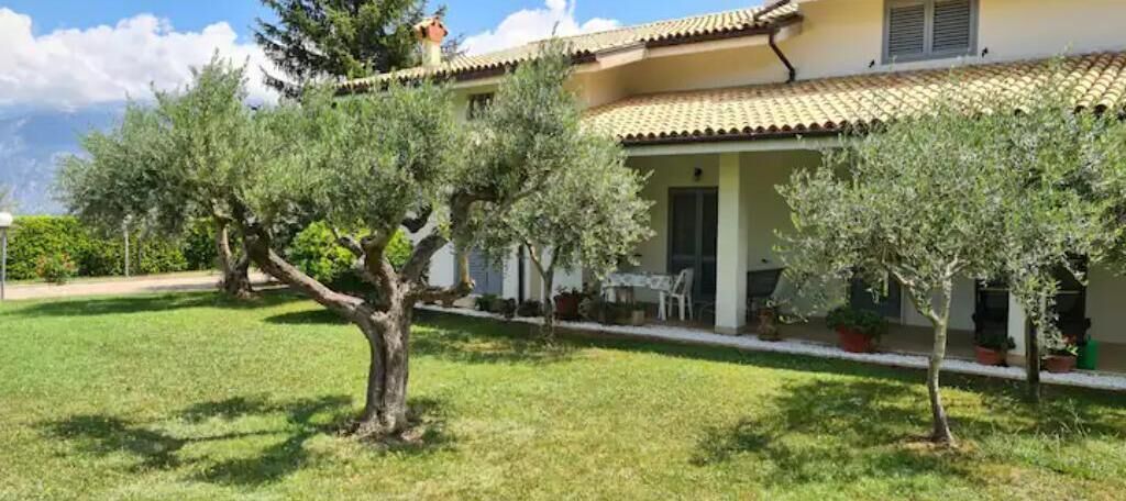 Une maison avec un toit en tuiles, un patio couvert et une pelouse bien entretenue agrémentée de plusieurs arbres.