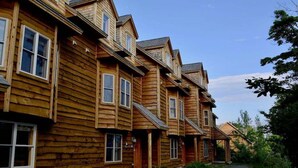 A row of wooden cabins with multiple windows and a gravel path leading to the entrance.
