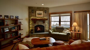 A cozy living room with a stone fireplace, a bookshelf, a sofa, and a window with curtains.