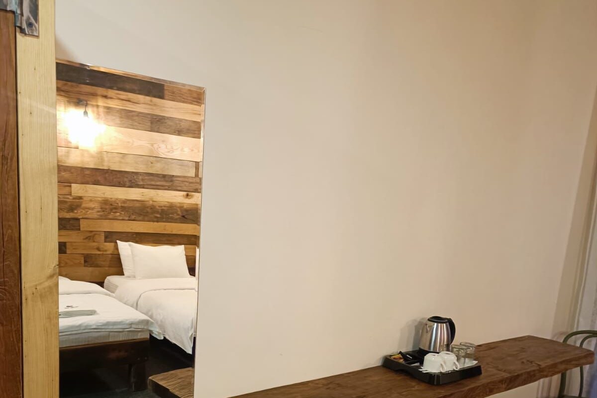 Una habitación con una cama, un estante de madera con una cafetera y un cubo de basura.