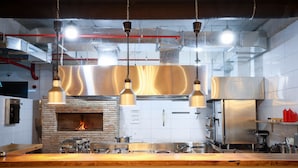 Uma cozinha moderna com forno de tijolos, eletrodomésticos de aço inoxidável, luminárias pendentes e bancada de madeira.