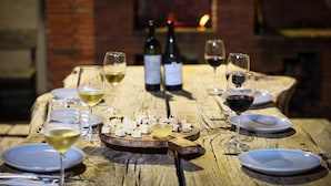 Mesa de madeira posta para refeição, com pratos, copos e tábua de queijos.