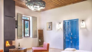 Quarto com cama, uma cadeira de madeira, uma mesinha com garrafa e copos, lareira e porta azul.
