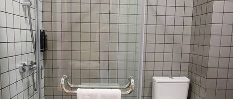 A bathroom with a glass-enclosed shower, a white toilet, and a tiled floor.