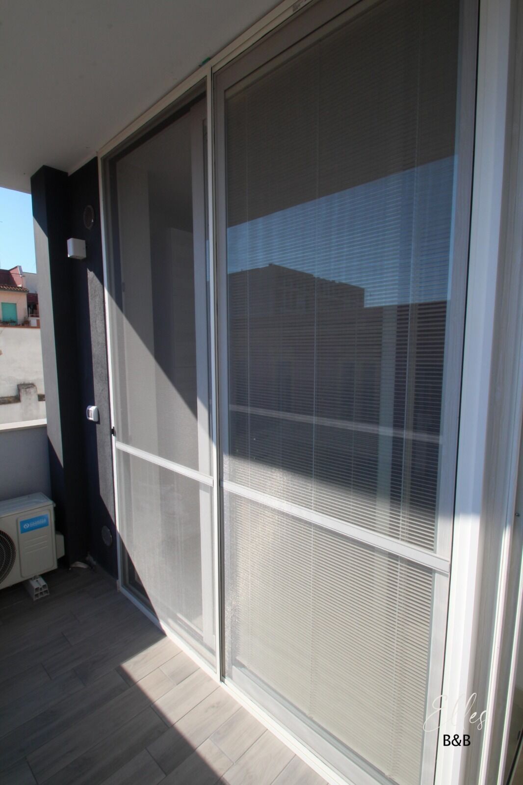 Een glazen schuifdeur met een metalen hor, een klein airconditioningsysteem en een houten vloer.