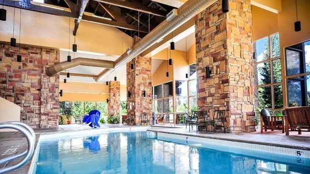 An indoor swimming pool with stone pillars, large windows, and outdoor seating.