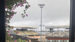 Een stadion met meerdere rijen zitplaatsen, een hoge lichtmast en een stenen muur.