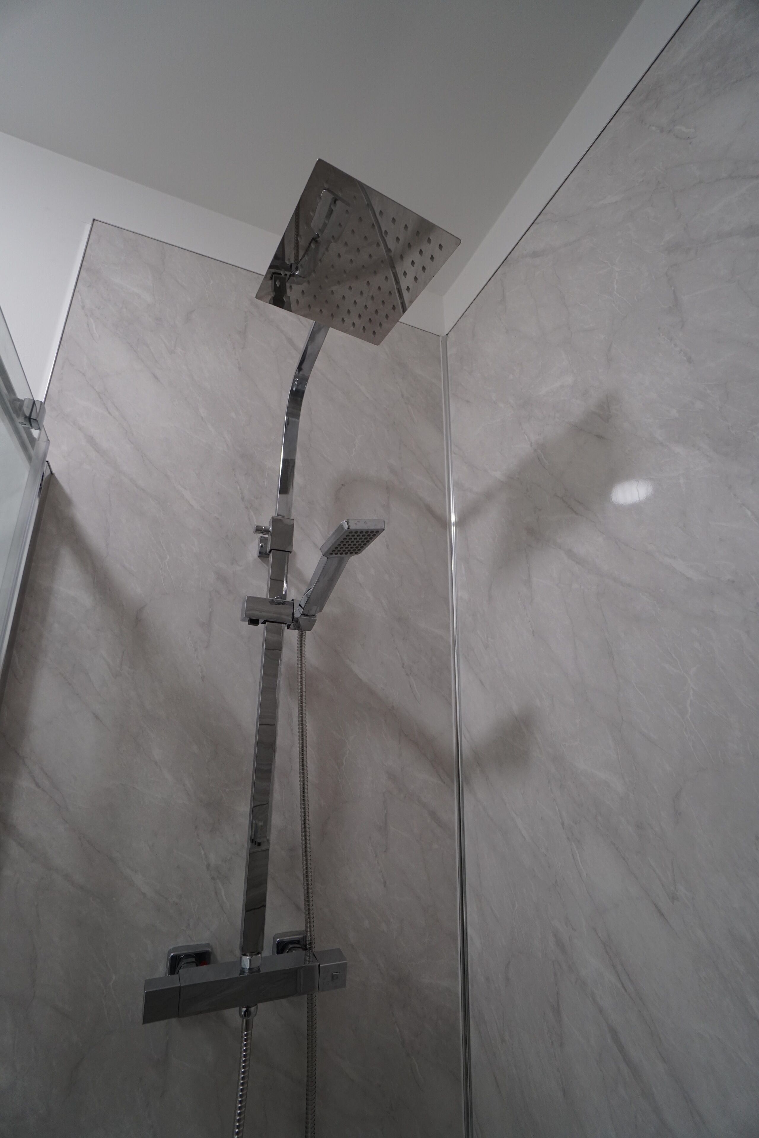 Une douche moderne dotée d’un pommeau de douche carré et d’un pommeau de douche à main.