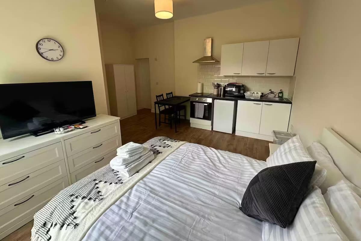 A compact hotel room with a bed, a TV, a small kitchenette, and a dining area.