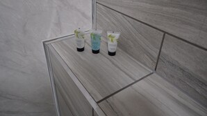 Une salle de bain avec un mur en marbre et un meuble-lavabo en bois. On y trouve trois articles de toilette sur le meuble-lavabo.