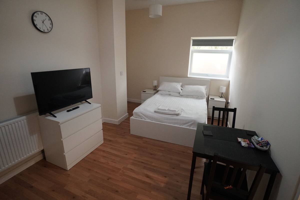 A bedroom with a bed, a TV on a dresser, a window, and a table.