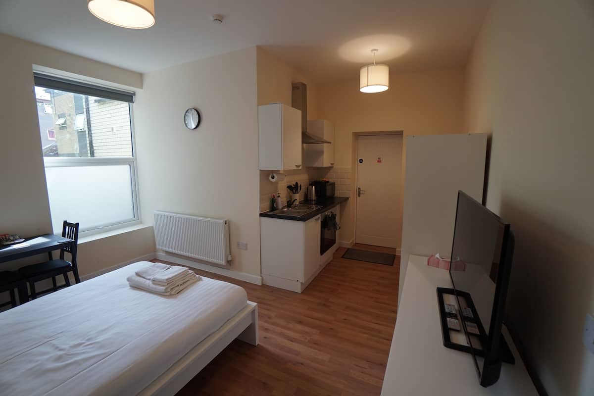 A compact room with a bed, a small kitchenette, a TV, and a window.