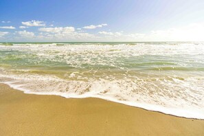 A beach with waves gently lapping onto the shore under a clear sky. - Tropical Beach Oasis - Coral (Cape Canaveral)