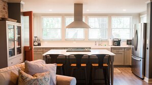 A modern kitchen with a central island, bar stools, a built-in oven, and a stainless steel refrigerator. - Charming 1920's House - pet friendly, 45 minutes from beach & attractions! (Sanford)