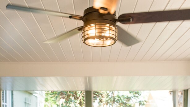 A dining table set with plates, glasses, and a bowl of fruit, surrounded by wicker chairs, under a ceiling fan. - Charming 1920's House - pet friendly, 45 minutes from beach & attractions! (Sanford)