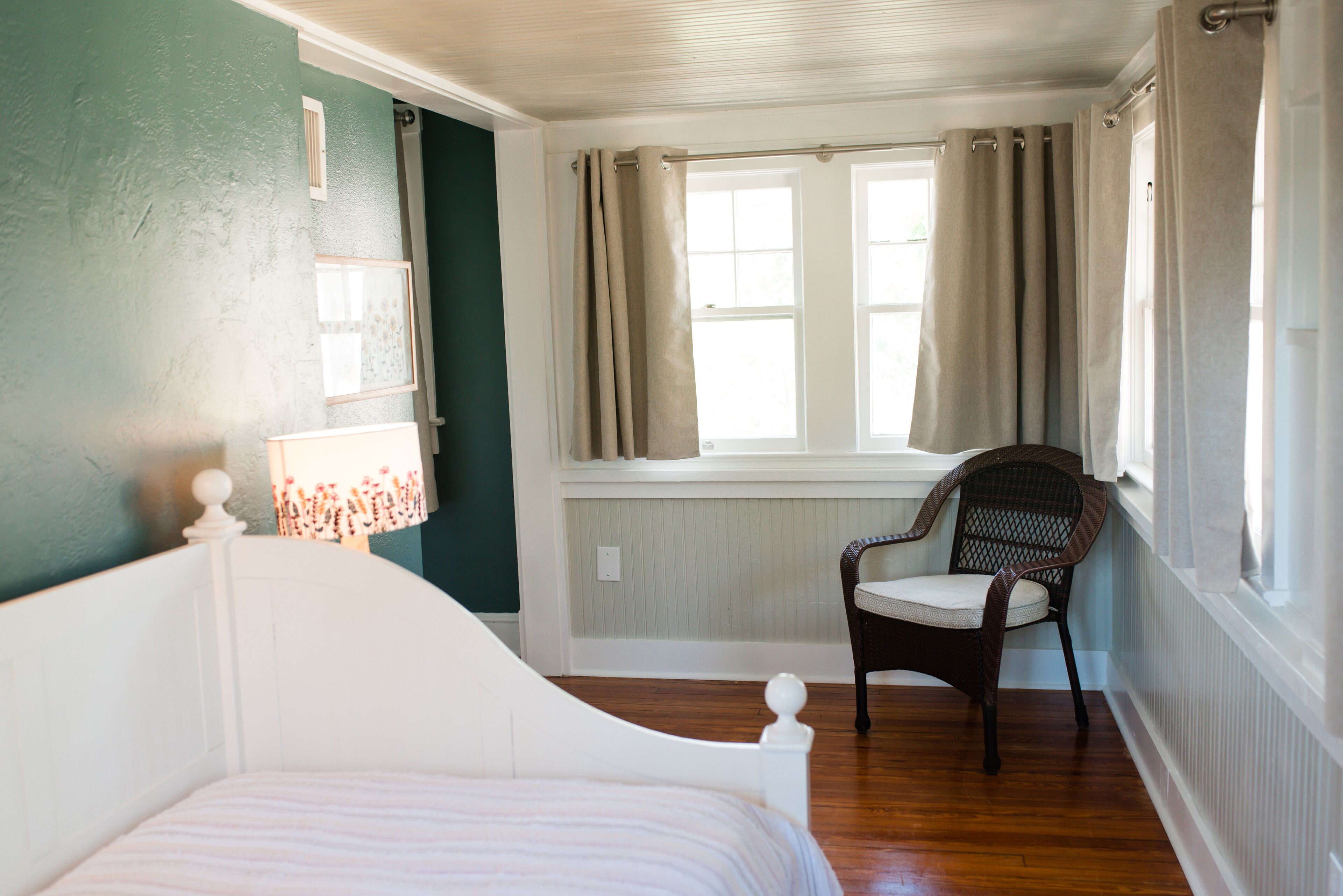 Une chambre avec un lit blanc, une chaise, une fenêtre avec des rideaux et un mur à la finition texturée.
