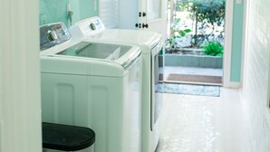A laundry area with a washing machine and dryer, a trash can, and a door leading to a garden. - Charming 1920's House - pet friendly, 45 minutes from beach & attractions! (Sanford)