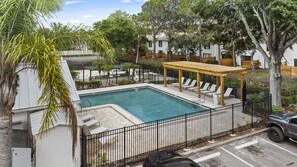 Una piscina con sillas de descanso y una pérgola, rodeada por una valla y árboles.
