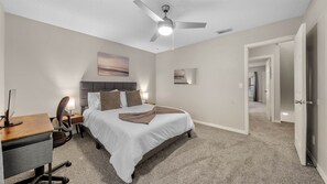 Un dormitorio con cama, escritorio, silla y ventilador de techo.