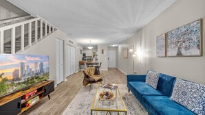 Un salón amplio con un sofá azul, una mesa de centro y un televisor que muestra una vista urbana.