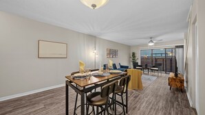 Un comedor amplio con una mesa y sillas de madera, un sofá y vistas al exterior a través de amplios ventanales.