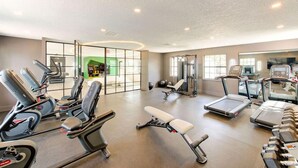 Un gimnasio con diversos equipos de ejercicio, incluyendo cintas de correr, elípticas y bancos de pesas.