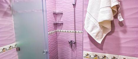 A bathroom with pink tiled walls, a glass shower enclosure, a white towel hanging on the wall, and a marble floor.
