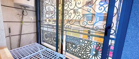 A balcony with a metal grill table, decorative metalwork, and a view of buildings through a glass door with intricate patterns.