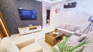 A modern living room with a flat-screen TV, a sofa, a coffee table, and decorative plants. - Elite Holiday Homes - Luxury & Centric Flat (Tangier)