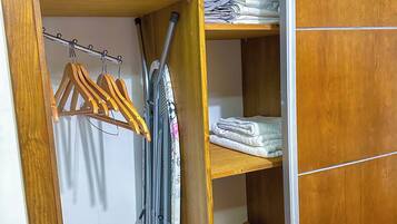 A wooden wardrobe with a mirror, a hanging rack with clothes, and a folded towel on the top shelf.
