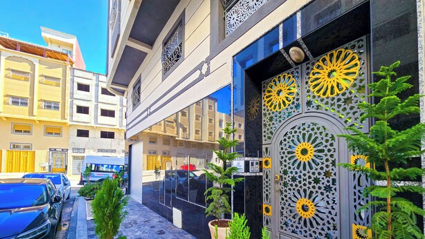 A building with a large decorative door, potted plants, and parked cars. - Elite Holiday Homes - Luxury & Centric Flat (Tangier)