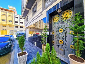 Un edificio con una puerta decorativa grande, plantas en macetas y automóviles estacionados.