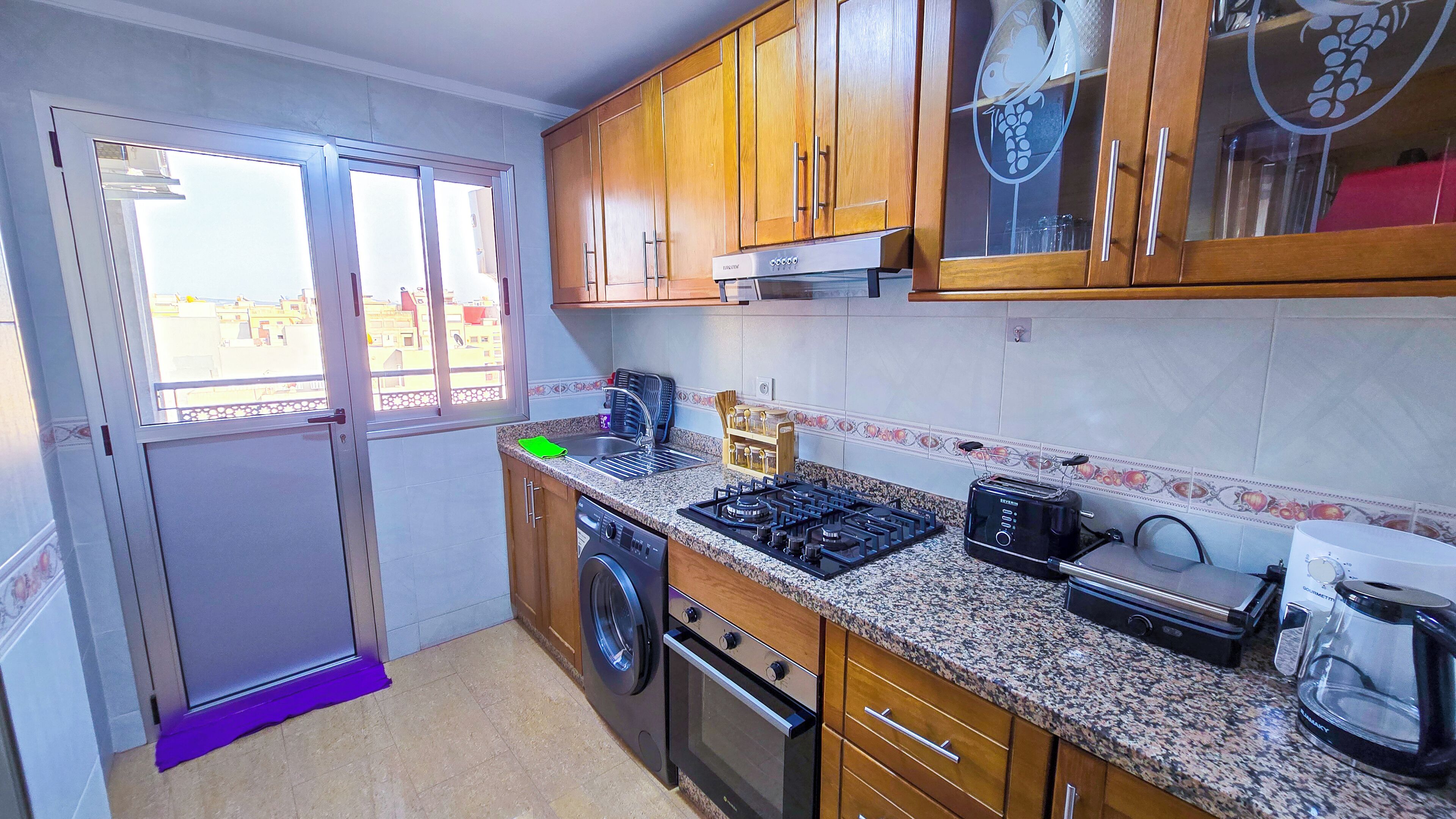 Una cocina compacta con armarios de madera, horno empotrado, cocina a gas, tostadora y cafetera.