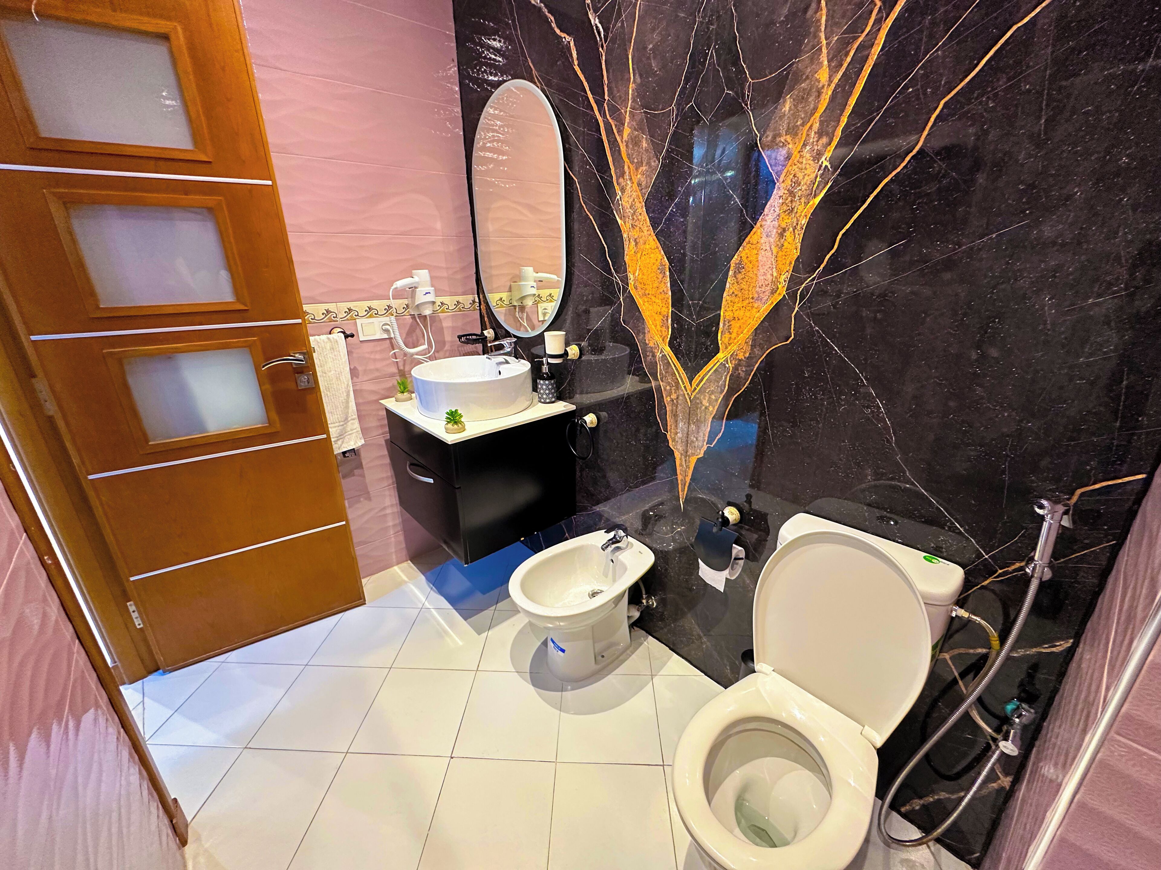 Une salle de bain comprenant des toilettes, un bidet, un meuble-lavabo avec un miroir et un évier.