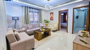 A modern living room with a sofa, armchairs, a coffee table, and a TV. - Elite Holiday Homes - Luxury & Centric Flat (Tangier)