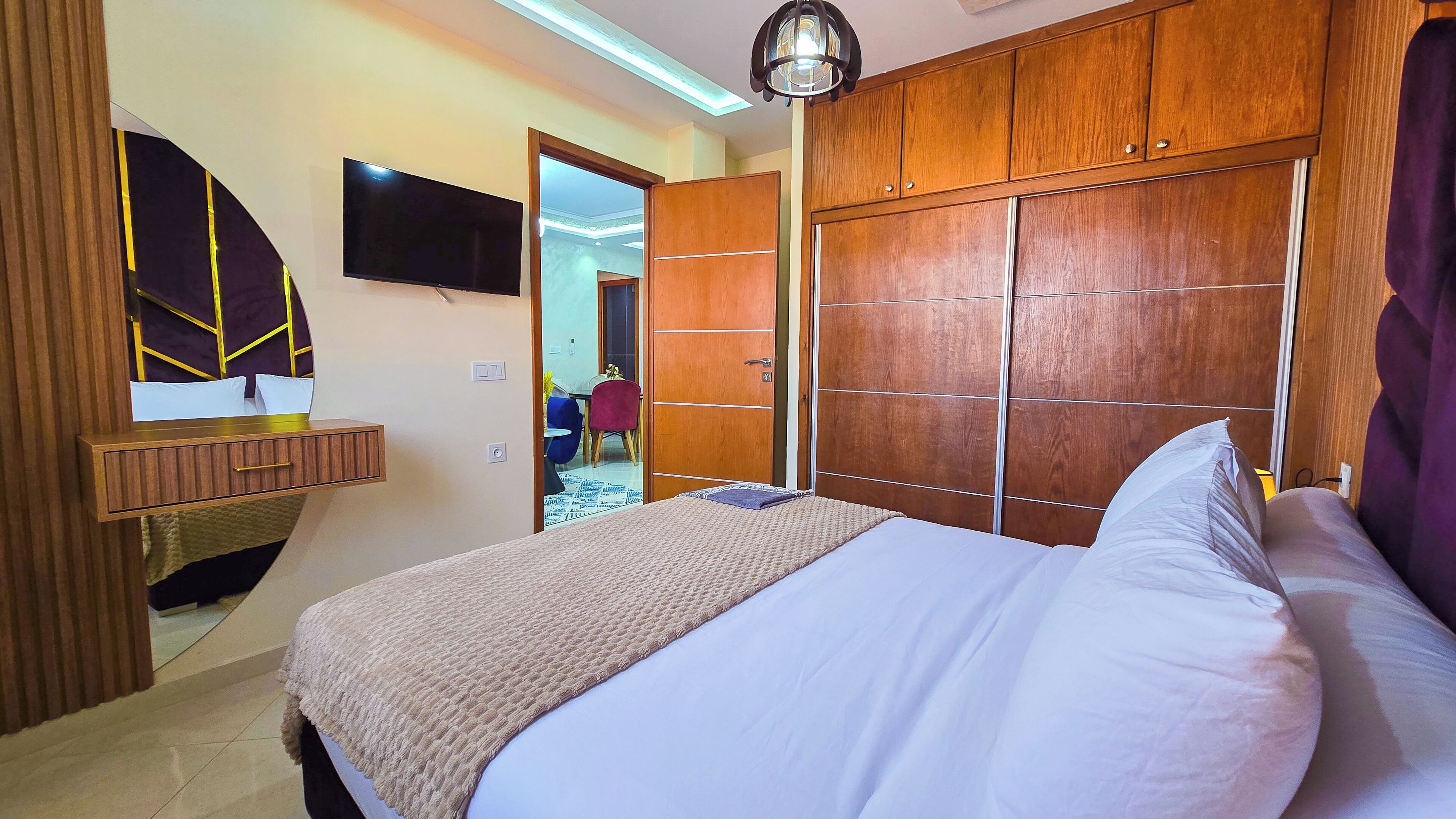Una camera d'albergo con un letto, un armadio in legno, una TV a schermo piatto e uno specchio.