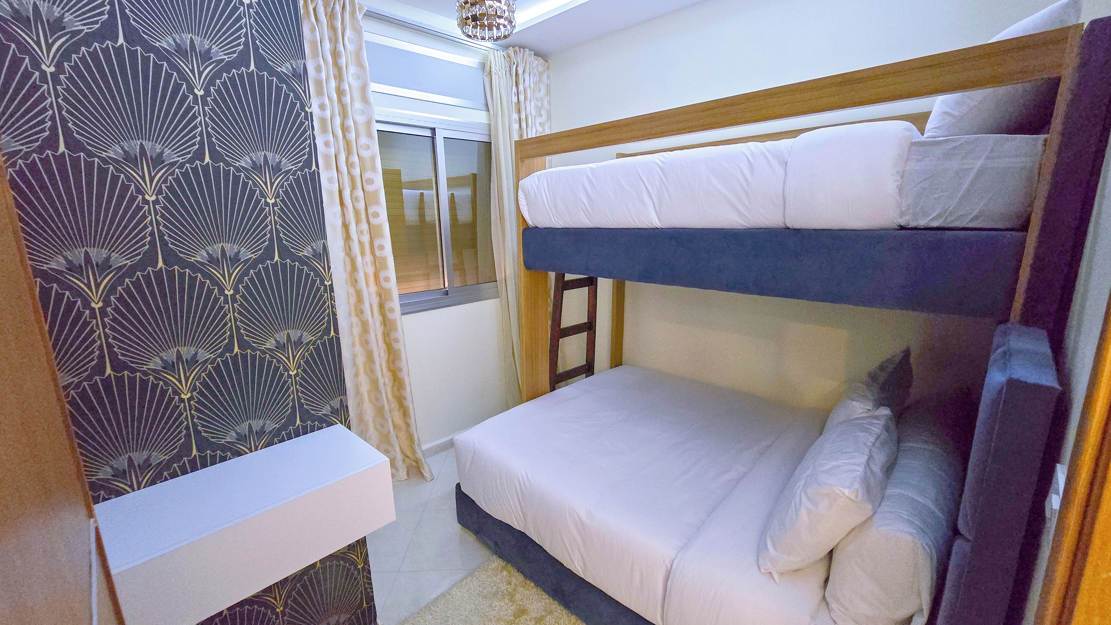 A bunk bed room with a window, curtains, and a patterned wallpaper.